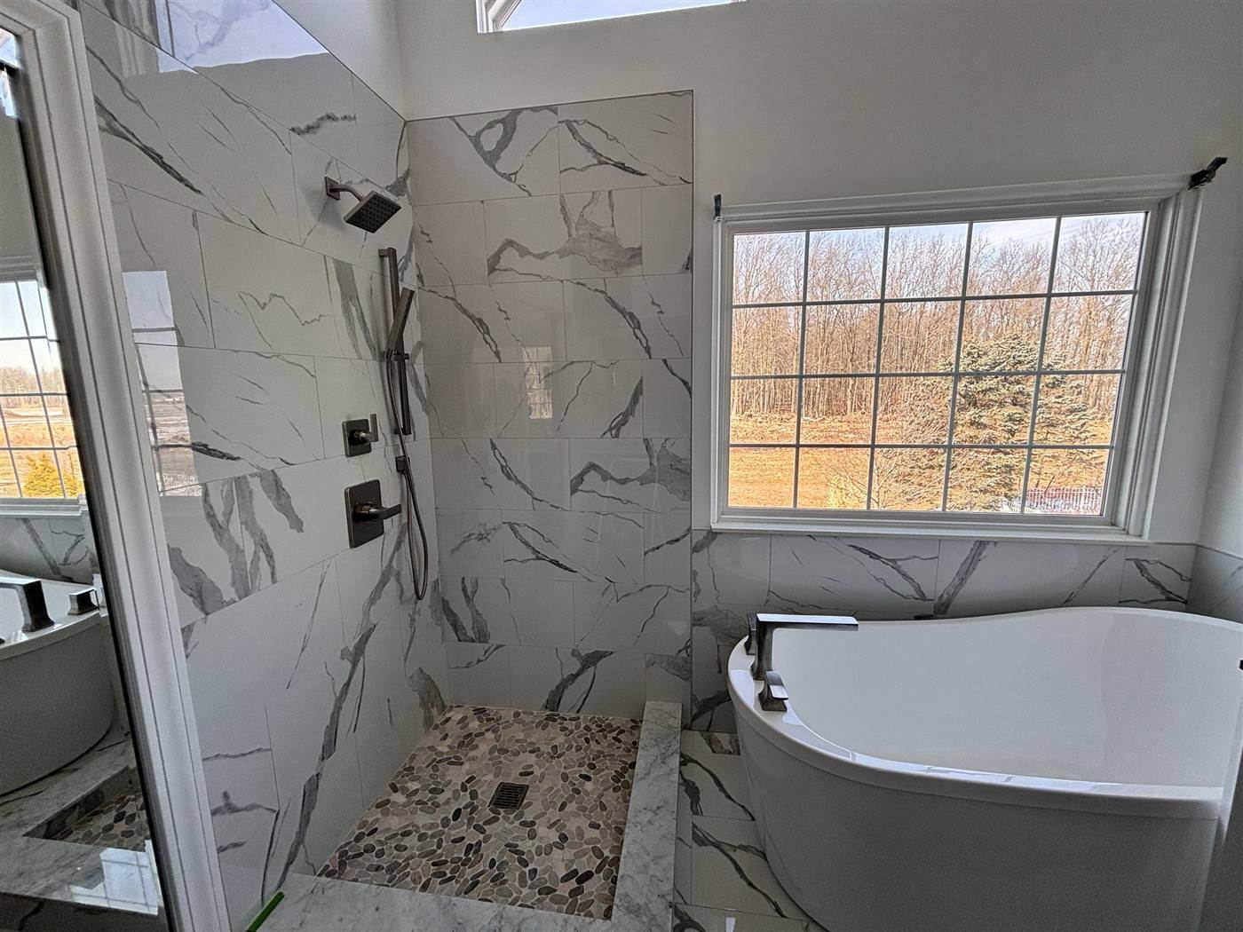 Walk-in shower with marble-look tile and a pebble floor