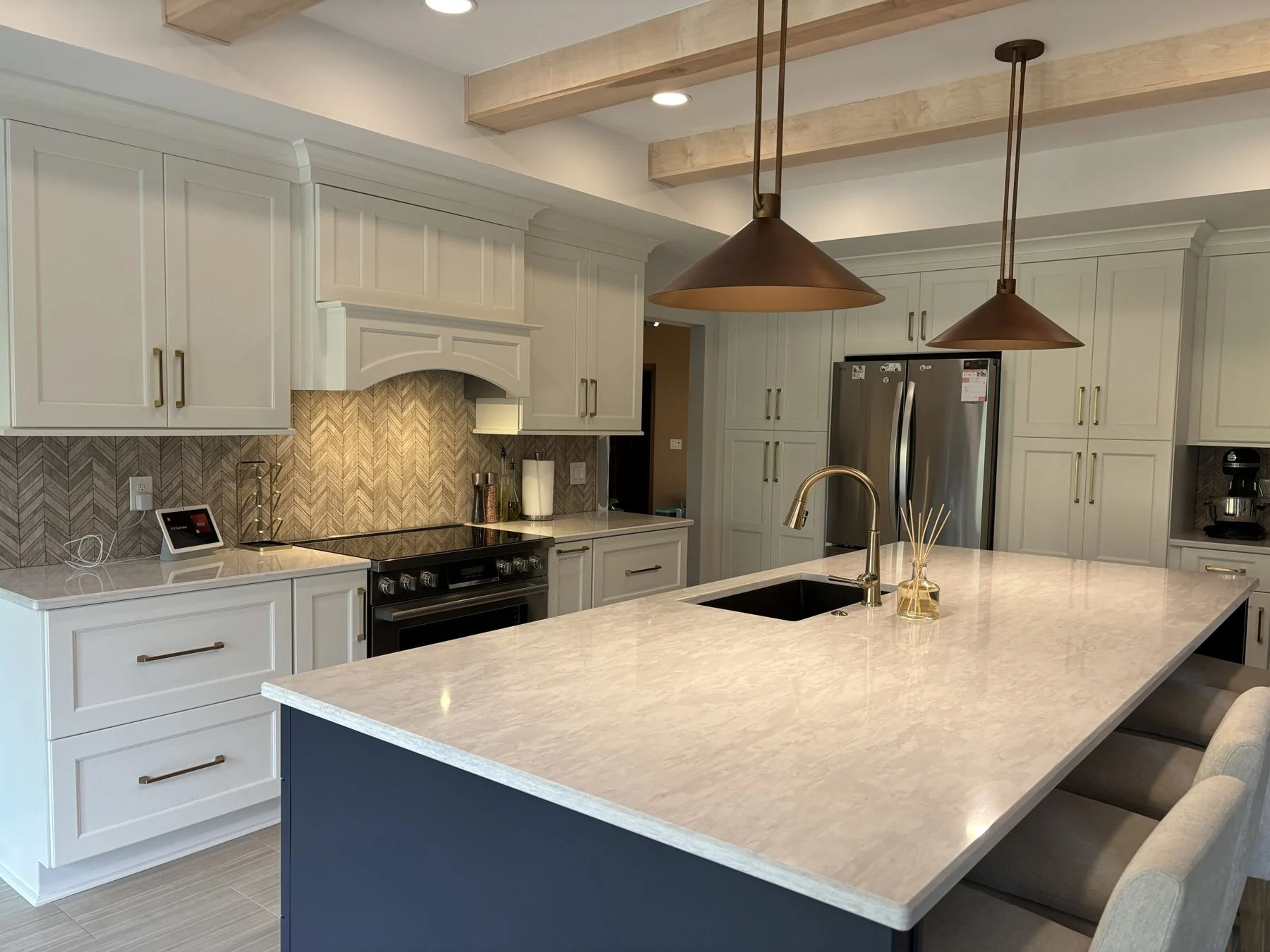 Kitchen remodeled by HomeWorks with a navy island, copper pendants and wood ceiling beams